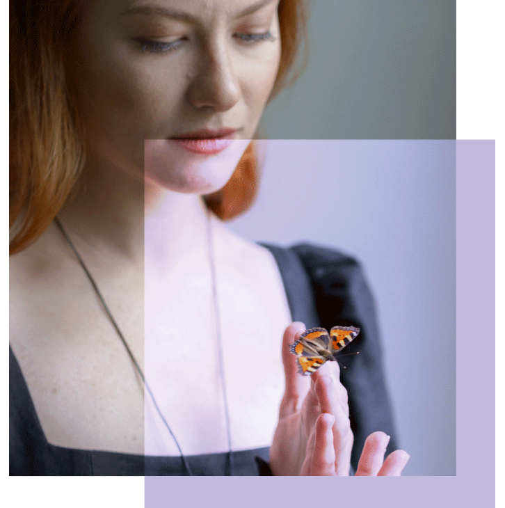 Jeune femme rousse qui contemple un papillon sur le bout de ses doigts.